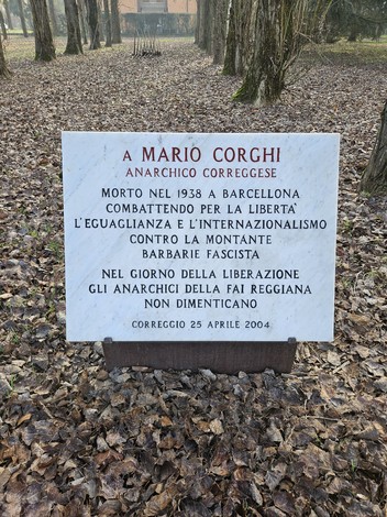 Lapide commemorativa a Mario Corghi, anarchico, situata in un ambiente boschivo.