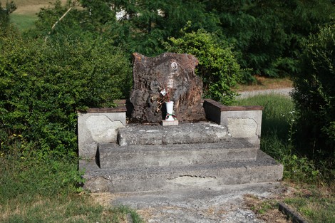 Monumento a Osti, semplice struttura in pietra con piante verdi circostanti e un'area ben curata.