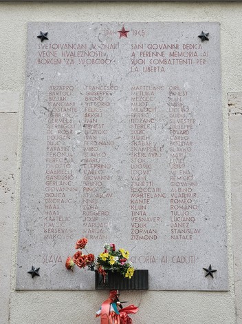 Lapide commemorativa in onore dei caduti per la libertà, con nomi incisi e decorazioni floreali.