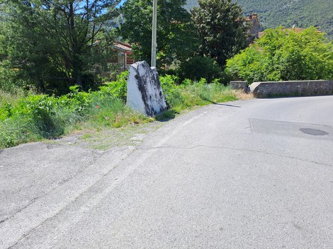 Cippo a Pacchini situato lungo una strada, circondato da vegetazione e elementi naturali.
