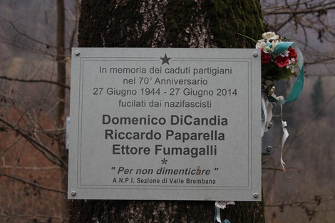 Targa commemorativa in memoria dei caduti partigiani con nomi e decorazioni floreali.