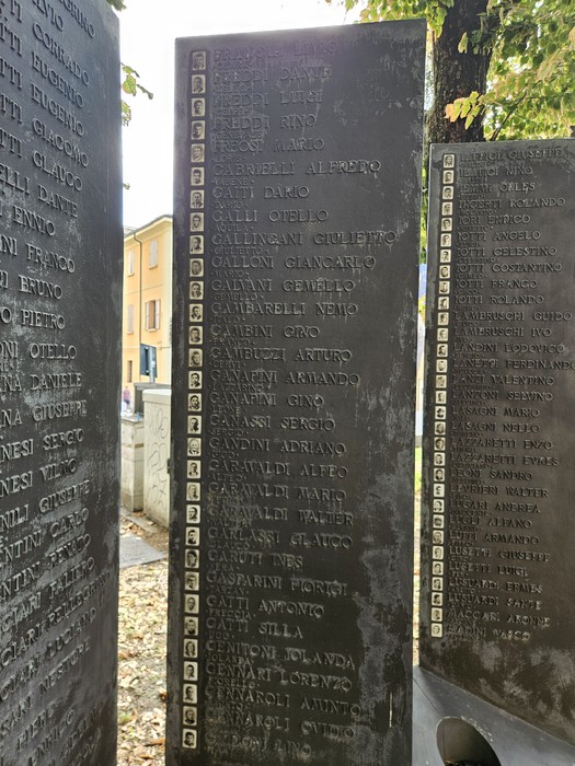 Pannello in pietra inciso con nomi e ritratti, parte del Sacrario della Resistenza Reggiana, in uno spazio alberato.