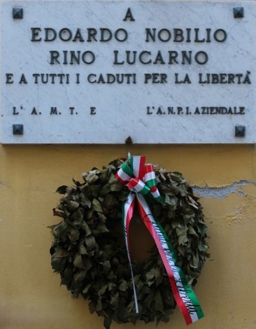Lapide dedicata a Edoardo Nobilio e Rino Lucarno, con una corona di alloro decorata da nastri tricolore.