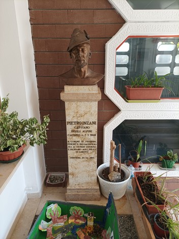 Busto di Pietronzano, scultore, con base decorata e piante in un ambiente interno.