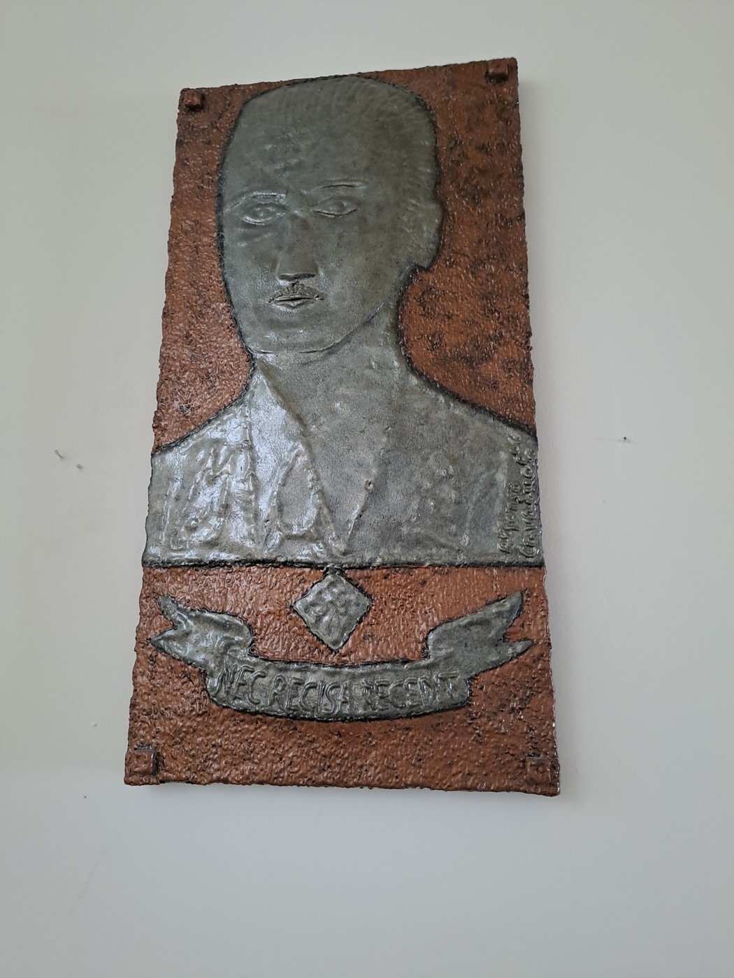 Lapide commemorativa con rilievo di un volto, dedicata a un evento storico significativo.