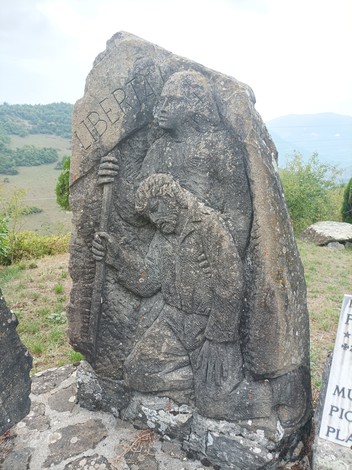 Monumento ai caduti con sculture che simboleggiano libertà e sacrificio, immerso in un paesaggio verde.