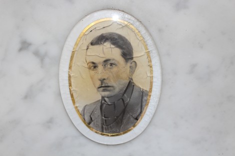 Ritratto di un uomo storico, incorniciato con un bordo dorato su sfondo marmoreo.