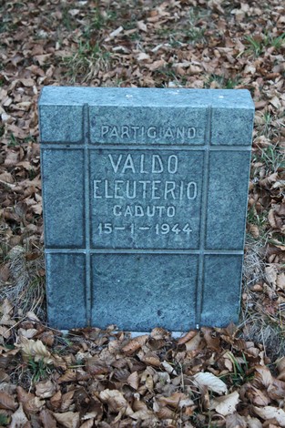 Cippo commemorativo dedicato a Valdo Eleuterio, partigiano caduto nel 1944, circondato da foglie secche.