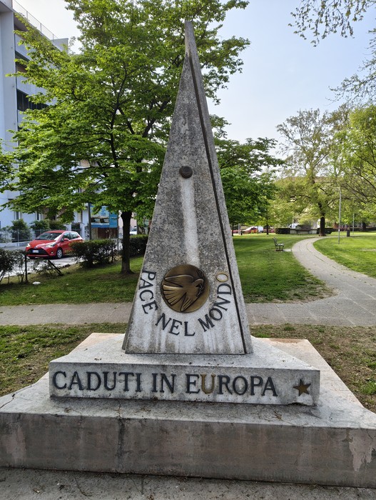 Monumento ai caduti con obelisco in marmo, incisi messaggi di pace e commemorazione in un parco.