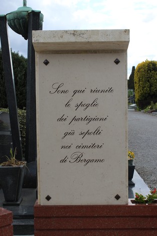 Monumento commemorativo dedicato ai partigiani, situato in un cimitero di Bergamo, circondato da vegetazione.