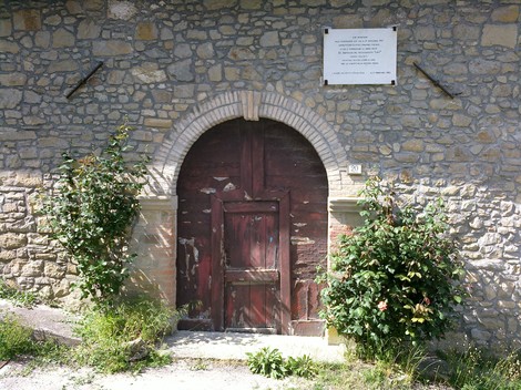 Lapide commemorativa per i partigiani di Lagoreccio, situata su un muro di pietra accanto a un portone.