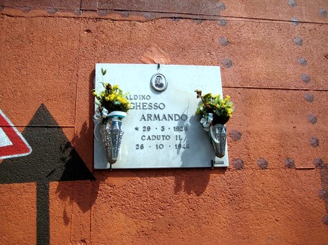 Lapide commemorativa in memoria di Armando Meneghesso, decorata con fiori e collocata su un muro.