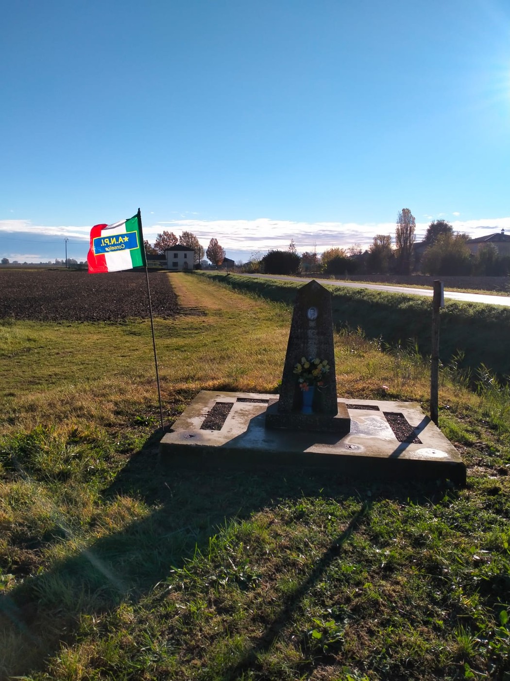 Cippo a Guidi con bandiera italiana, in un paesaggio rurale sereno e soleggiato.