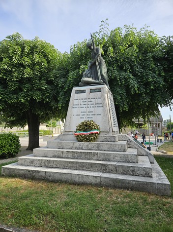 Monumento ai Caduti di Solarolo Rainerio, con una statua su base monumentale, circondato da vegetazione.