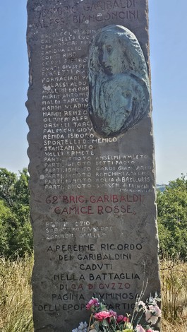 Stele commemorativa dedicata alla "62ª Brigata Garibaldi", situata a Ca' di Guzzo, circondata da fiori.
