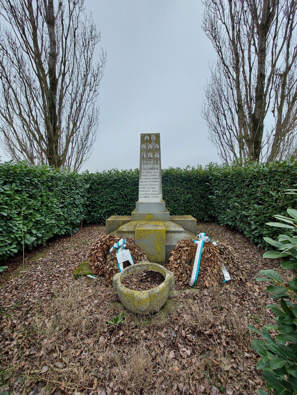 Monumento commemorativo dedicato alle vittime dell'eccidio del Palazzone, circondato da siepi e decorato con corone.