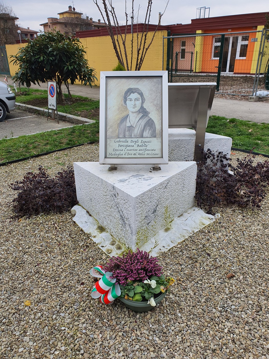 Monumento a Degli Esposti con ritratto e decorazioni floreali in un contesto urbano.