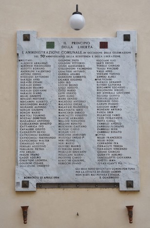 Lapide commemorativa che onora i caduti, con nomi incisi su marmo, situata in un contesto pubblico.