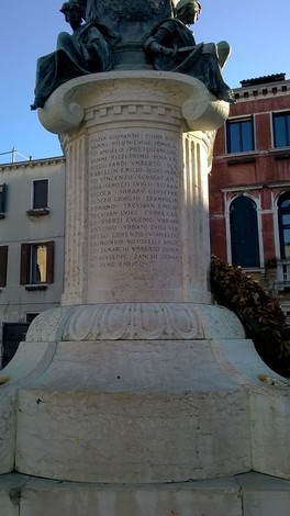 Monumento ai caduti dei Carmini, con iscrizioni commemorative e statue sullo sfondo di edifici storici.