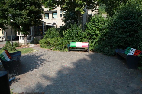 Panchine decorate con i colori della bandiera italiana, immerse in un'area verde urbana.