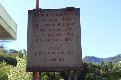 Lapide commemorativa dedicata alle vittime del bombardamento, con sfondo di alberi e cielo sereno.