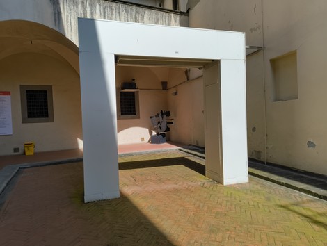 Scorcio di un cortile con una scultura al centro, incorniciata da un portico bianco in un ambiente luminoso.