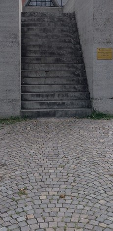 Scalinata di cemento che conduce al "Monumento ai Partigiani", circondata da pavimentazione in ciottoli.