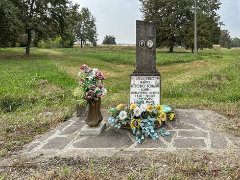Cippo commemorativo dedicato a Lelli e Bonacini, adornato con fiori, immerso nel verde.