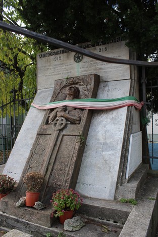 Monumento decorato con epigrafi in ricordo dei caduti, con piante e drappi tricolore.