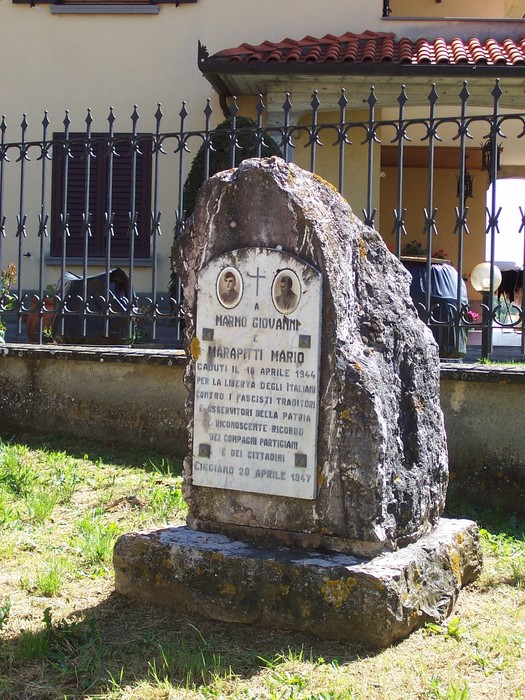 Cippo commemorativo in marmo dedicato a Mario Marapitti, situato in un'area verde e affacciato su una recinzione.