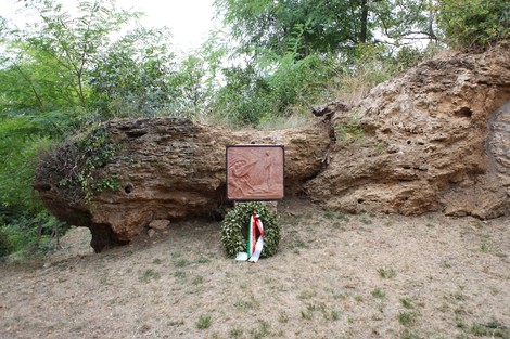 Monumento a Don Bortolotti, affiancato da una corona di fiori, in un contesto naturale e roccioso.