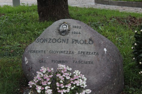 Cippo commemorativo dedicato a Paolo Sonzogni, con foto e data, circondato da fiori.