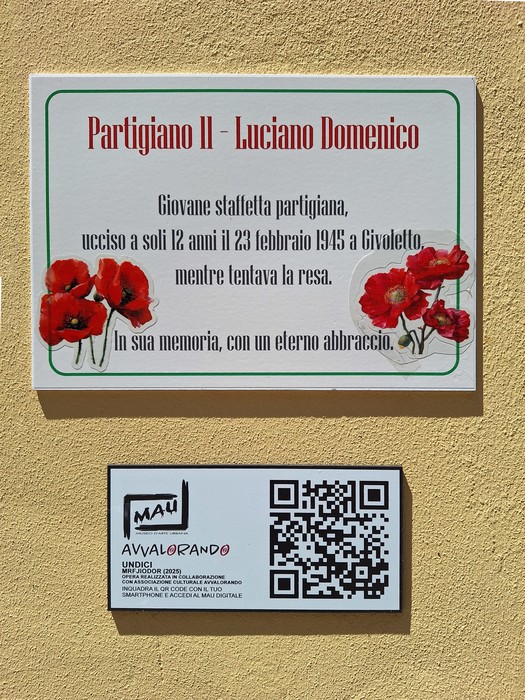 Murale dedicato a Luciano Domenico, partigiano, con fiori rossi e un codice QR, su sfondo giallo.