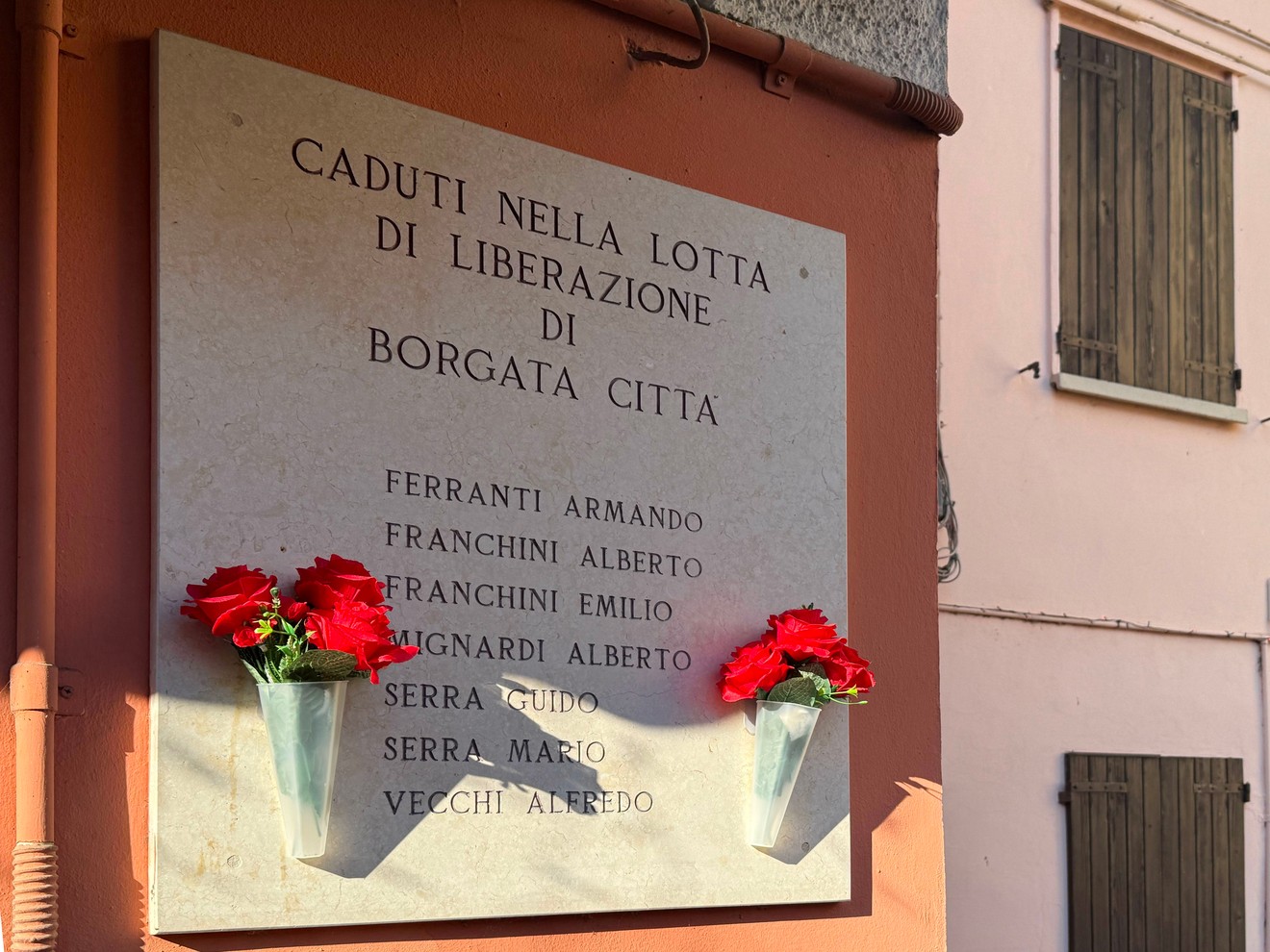 Lapide commemorativa dedicata ai caduti della lotta di liberazione a Borgata Città, adornata con fiori.