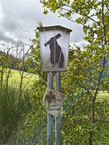 Monumento della Via Crucis di Casaglia, con un segno di croce e un'immagine di Gesù, circondato dalla natura.