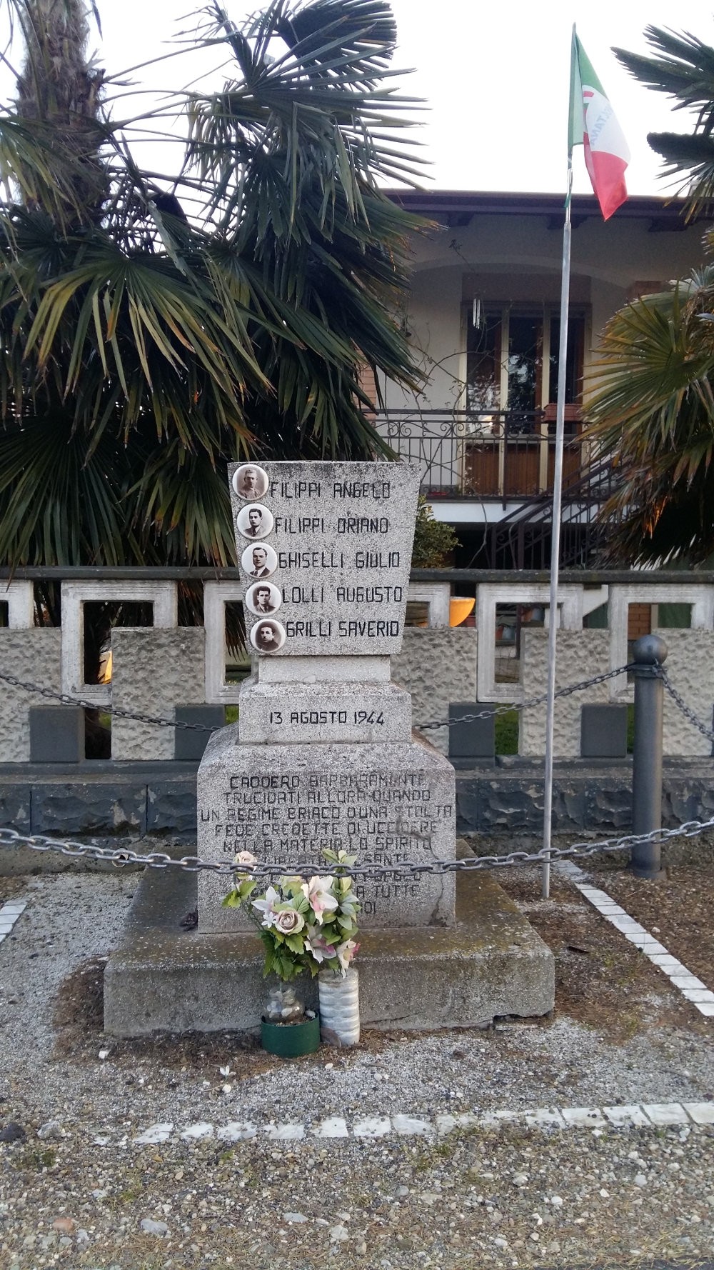 Monumento ai Cinque Martiri, commemorazione di figure storiche, con fiori freschi e bandiera italiana sullo sfondo.