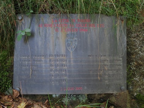 Memoriale di una fossa comune con targa commemorativa e nomi delle persone scomparse. Ambiente naturale circostante.