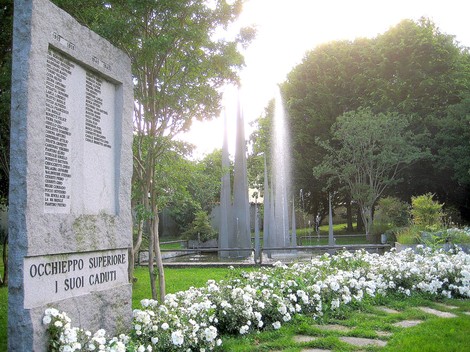Monumento ai caduti di Occhieppo Superiore, circondato da un giardino fiorito e giochi d'acqua.