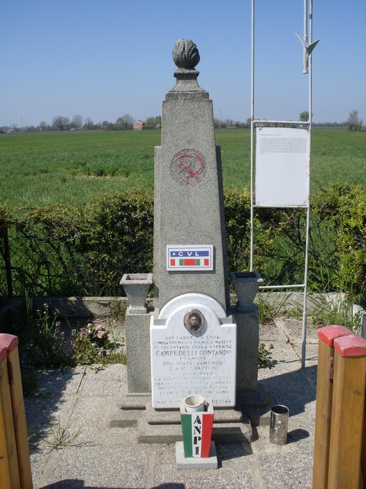Cippo commemorativo a Campedelli, dedicato ai caduti, circondato da un paesaggio verde e sereno.