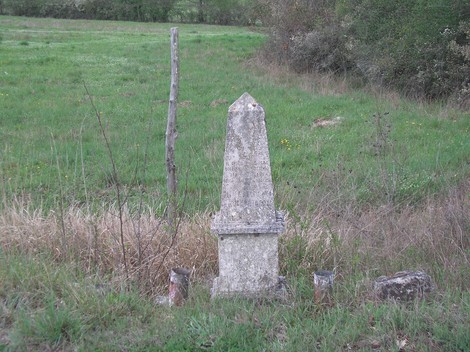 Cippo in pietra dedicato a Periccioli e Taddei, immerso nel verde di un campo aperto.