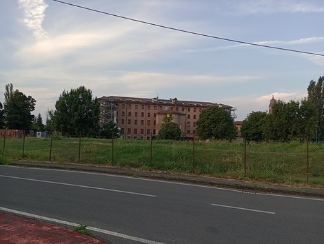 Lapide del campo di prigionia PG 49, con struttura storica sullo sfondo e verde circostante.