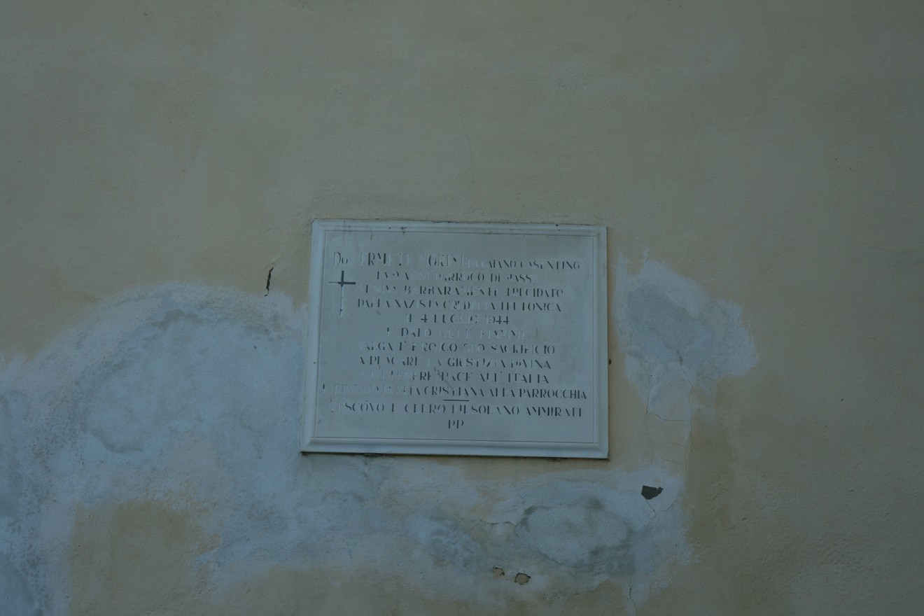 Lapide commemorativa a Don Morini, visibile su un muro. Riconoscimento della sua opera e dedicazione.