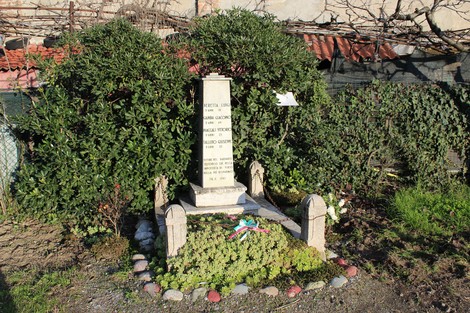 Monumento ai caduti dell'Insurrezione, circondato da vegetazione e adornato con fiori e decorazioni.