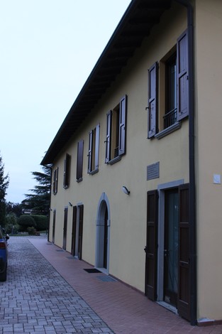 Edificio con facciata gialla e finestre con persiane, situato in un'area tranquilla e verdeggiante.