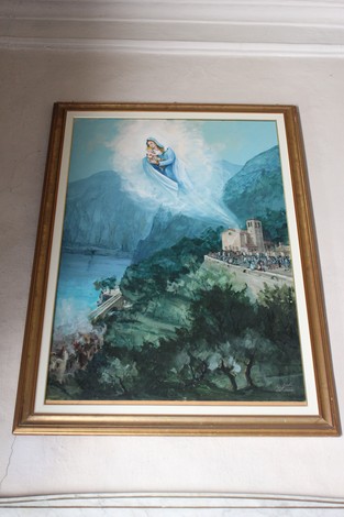 Lapide ex voto che raffigura la Madonna sopra un paesaggio montano e un antico edificio.