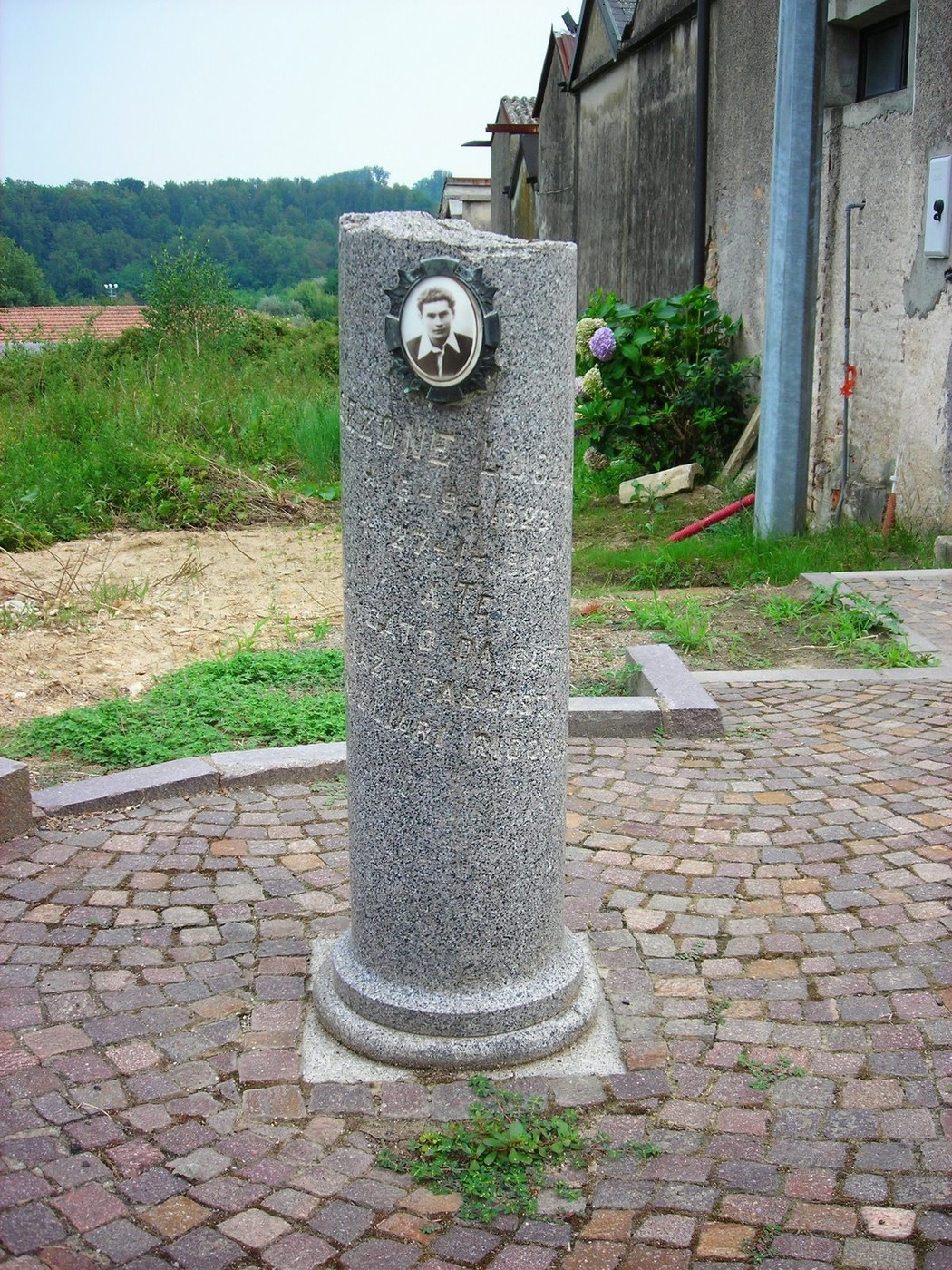 Cippo commemorativo in pietra con targa e scritte, situato in un'area verde e tranquilla.