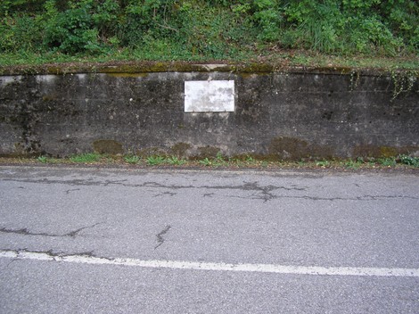 Lapide storica sul ponte del fiume Farma, immersa nel verde, vicino alla strada.