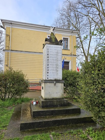Monumento ai Caduti di tutte le Guerre immerso nel verde, con un edificio storico sullo sfondo.