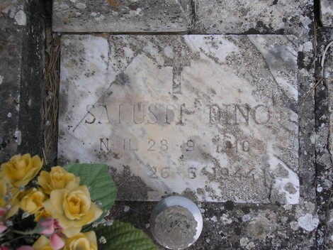 Lapide dedicata ai partigiani, con decorazioni floreali e scritte commemorative in un ambiente di memoria storica.