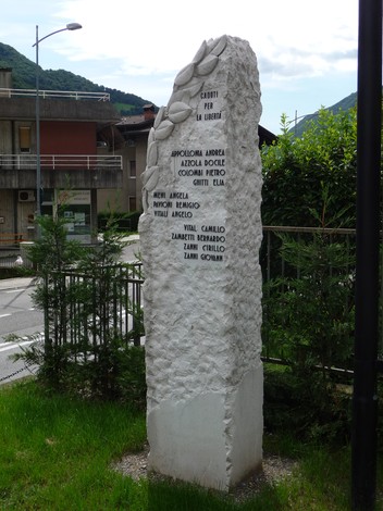 Monumento ai caduti per la Libertà, realizzato in pietra con nomi incisi, circondato da verde urbano.